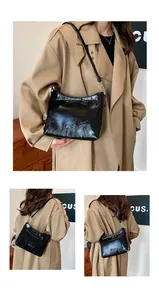Close-up of black glossy leather shoulder bag with pleated texture and metal hardware