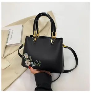 Detail of black tote with floral embroidery, gold V-hardware and leather handles