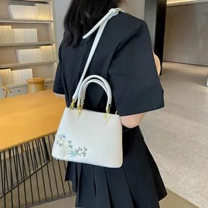 Minimalist beige tote bag with floral embroidery and gold V-shaped hardware accents