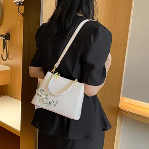 Minimalist white tote bag with floral embroidery shown on a model in a warm indoor setting
