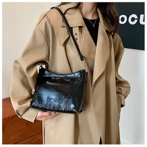 Close-up of black glossy pleated shoulder bag with sleek leather texture on khaki coat