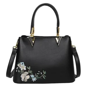 Minimalist black tote bag with floral embroidery and golden metal hardware on white background