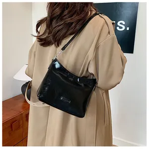 Detailed view of a black glossy shoulder bag styled with a classic khaki trench coat