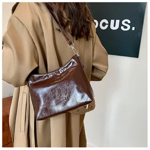 Detail of dark brown glossy leather shoulder bag worn with a stylish beige coat