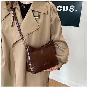 Detail of glossy brown leather shoulder bag with metallic buckle on beige trench coat