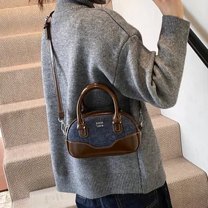 Retro denim bowling bag with brown leather trim shown in a stylish crossbody wear pose
