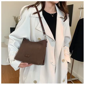 Model wearing dark brown square shoulder bag with matte finish and metallic detail