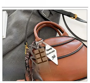 Detailed shot of brown crescent bag with crossbody strap and chocolate charm accessory