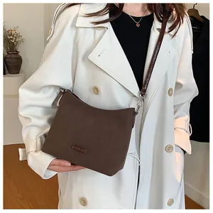 Close-up of a dark brown suede crossbody bag featuring the metallic Bella Luis brand logo