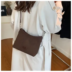 Detail of dark brown shoulder bag with sleek leather finish and silver hardware on model