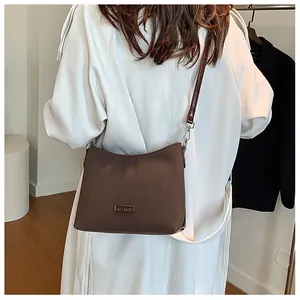 Brown suede crossbody bag with metal plaque on model in stylish white trench coat