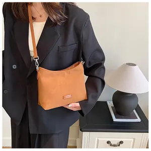 Detail of caramel suede-like shoulder bag with a metal logo tag and leather strap