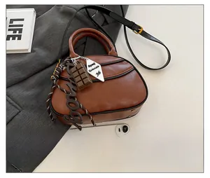 Brown leather baseball bag with charms next to a smartphone for size reference