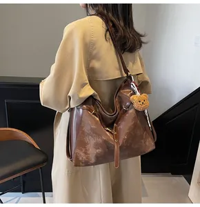 Detail of vintage brown tote bag with bear charm and silk scarf on a trench coat