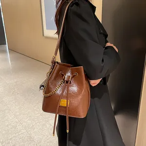 Sac seau en cuir marron avec chaîne dorée et breloque boule de billard porté