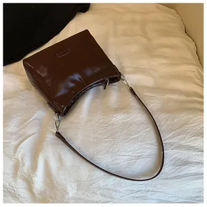 Detail of dark brown glossy patent leather shoulder bag with sleek metal zipper and logo