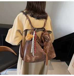 Detail of vintage brown leather backpack featuring a plush bear charm and woven cord decor
