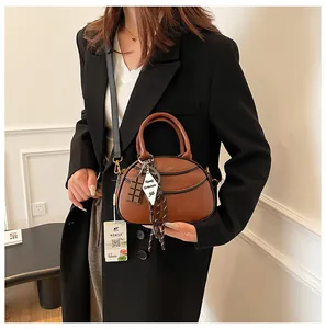 Detail view of caramel brown baseball-shaped crossbody bag with decorative charms and trim