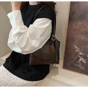 Detail of vintage oil-wax leather shoulder bag with golden buckles and keychain charm
