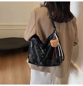 Detail of vintage black leather tote bag with plush bear charm and striped ribbon accent