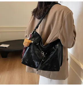 Model wearing a large black vintage tote bag with cracked texture and a plush bear charm