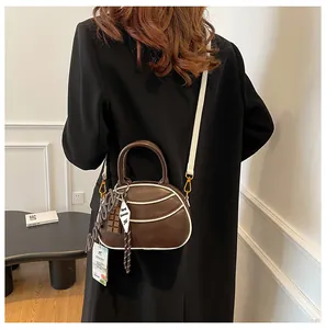 Detail of brown retro baseball bag with white trim and chocolate charm on a black coat