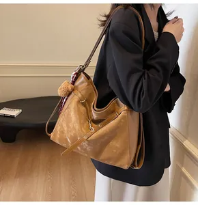 Close-up of caramel leather tote bag with plush bear charm and checkered ribbon