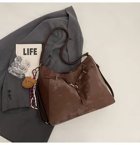Detail of dark brown vintage tote bag with gold buckle and plush bear charm on a grey suit