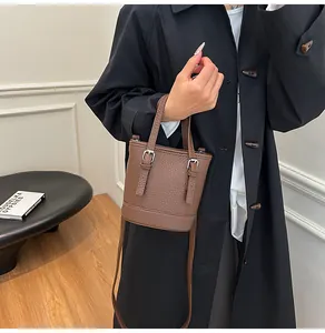 Detailed view of a brown pebbled leather bucket bag with top handles and shoulder strap