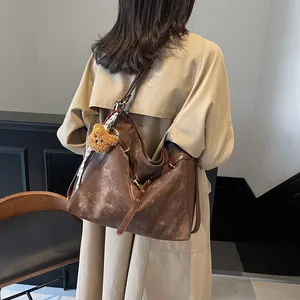 Vintage brown leather tote bag with plush bear charm worn with a classic trench coat