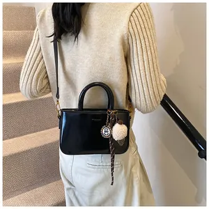 Détail d'un sac à main noir brillant chic avec charm pompon et boucle dorée élégante