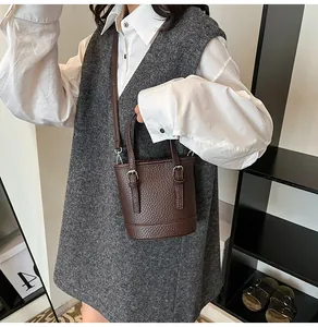 Close-up of dark brown lychee texture bucket bag with metal buckle detail on white shirt