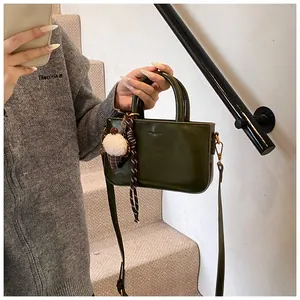 Détail d'un sac à main carré vert foncé avec texture brillante et breloque en peluche