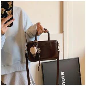 Détail du petit sac carré en cuir marron foncé avec pendentif crème glacée et bandoulière