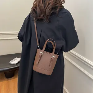 Brown litchi leather bucket bag shown as crossbody with stylish minimalist outfit