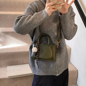 Sac à main boîte vert olive en cuir avec bandoulière et breloque sur escalier