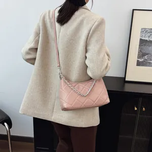 Pale pink quilted crossbody bag with silver chain strap worn by a model in interior
