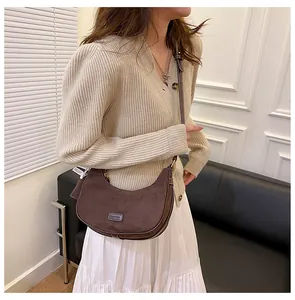 Detail of coffee brown suede crescent bag with Fashion logo patch and thin strap