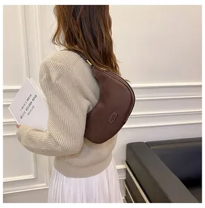 Detail of a brown matte leather crescent bag worn as a shoulder hobo bag on a model
