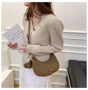 Detail of suede crescent bag with brown trim and mini coin purse charm on model