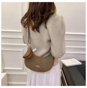 Brown suede crescent bag shown on model with adjustable strap and coin purse charm