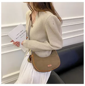 Brown frosted leather crescent bag with 'FASHION' embossed patch on cream knit cardigan