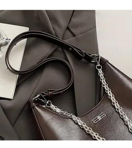 Detailed view of dark brown cracked leather bag with silver chain on grey blazer