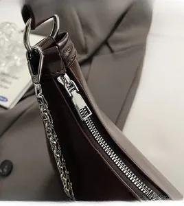 Detail of silver zipper closure and metallic chain on dark brown leather shoulder bag