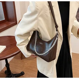 Model wearing dark brown underarm bag with silver chain and textured leather finish