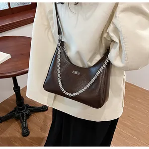 Detail of a dark brown hobo bag with a silver chain strap and metal logo on smooth leather