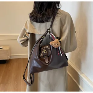 Detail of a large dark brown leather tote bag with buckle and plush bear charm on a model
