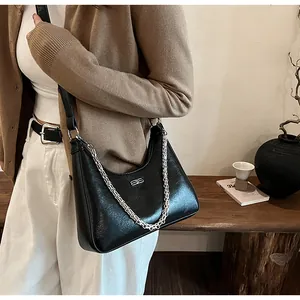 Detail of black glossy leather underarm bag with silver chain and metal logo accent