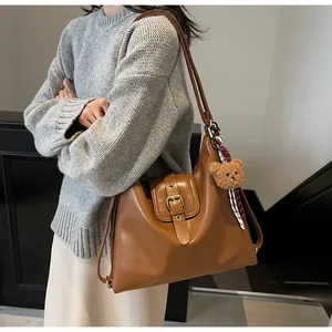 Detail of a brown leather hobo bag with a gold metal buckle and a plush bear charm