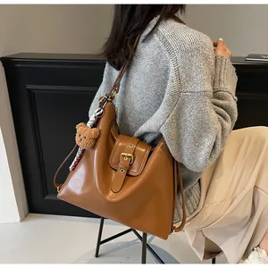 Detail view of brown leather shoulder bag with plush bear charm and plaid scarf accessory